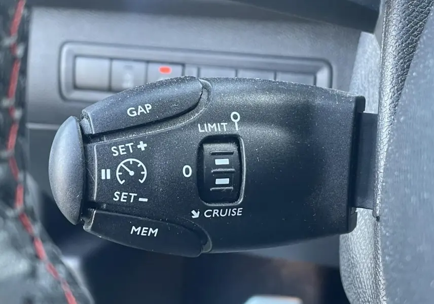 Gros plan sur la commande de régulateur de vitesse noire à gauche du volant d'une Peugeot 308 SW bleu Vertigo.