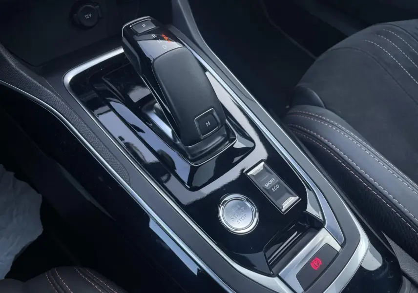 Gros plan sur la console centrale noire brillante de la Peugeot 308 SW 2021, avec levier de boîte auto et bouton start/stop.