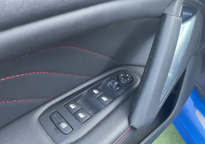 Gros plan sur la porte avant gauche d'une Peugeot 308 SW bleu Vertigo, avec commandes de vitres et surpiqûres rouges.