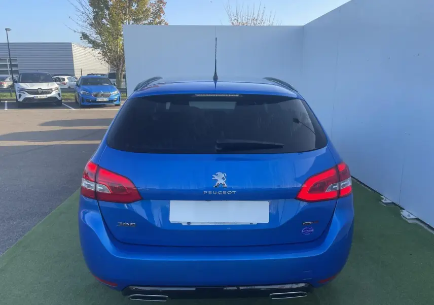 Vue arrière d'une Peugeot 308 SW bleu Vertigo avec double sortie d'échappement et vitres arrière surteintées.