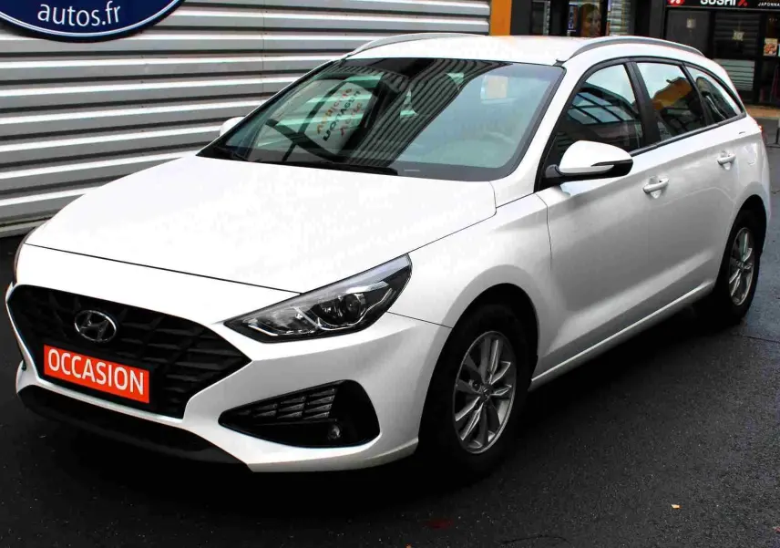 Hyundai i30 SW blanc polaire vue 3/4 avant droit, avec calandre noire et plaque "OCCASION" rouge visible.
