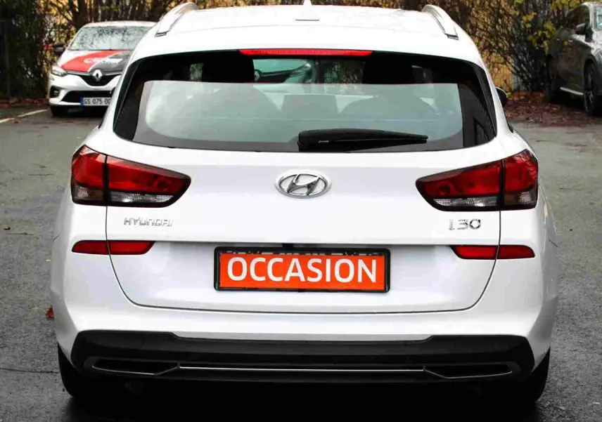 Vue arrière d'une Hyundai i30 SW blanche polaire avec plaque "OCCASION" en orange sur un parking extérieur.