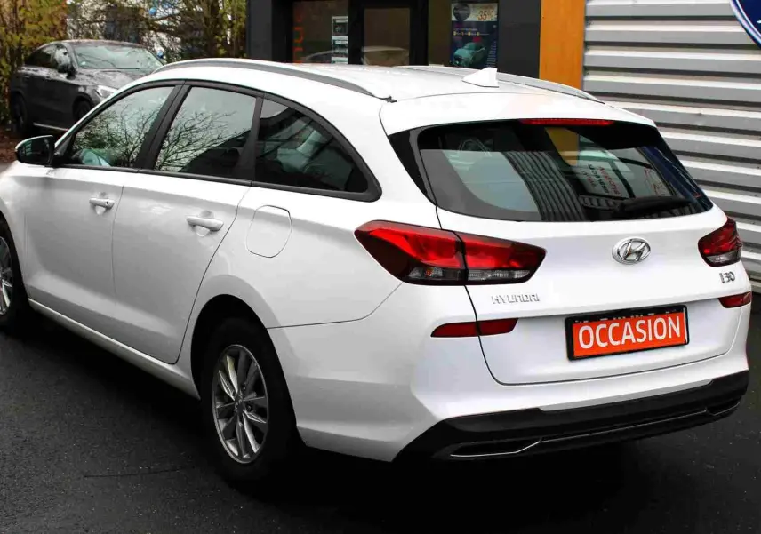 Vue 3/4 arrière droite d'une Hyundai i30 SW blanche polaire avec feux arrière LED et plaque "OCCASION" visible.