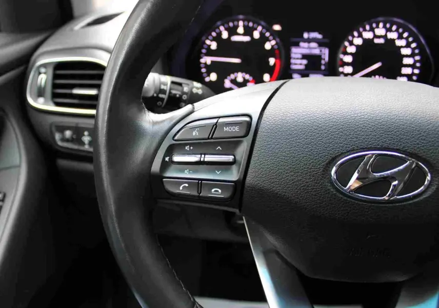 Gros plan sur le volant noir de la Hyundai i30 SW 2022 avec commandes audio et tableau de bord éclairé en arrière-plan.