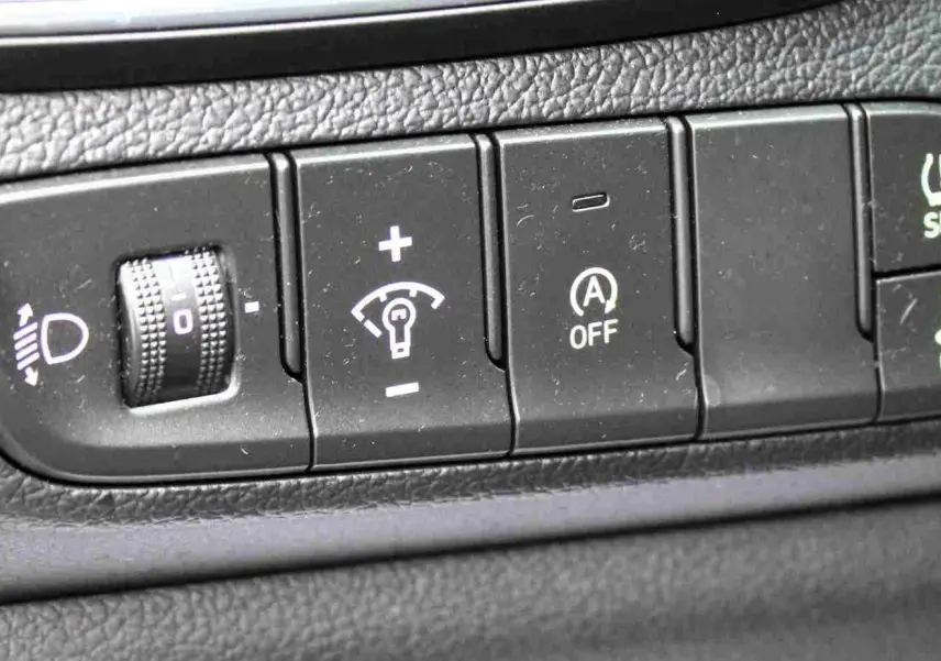 Gros plan sur les commandes de réglage d'éclairage, d'assistance et de sécurité du tableau de bord d'une Hyundai i30 SW blanche.