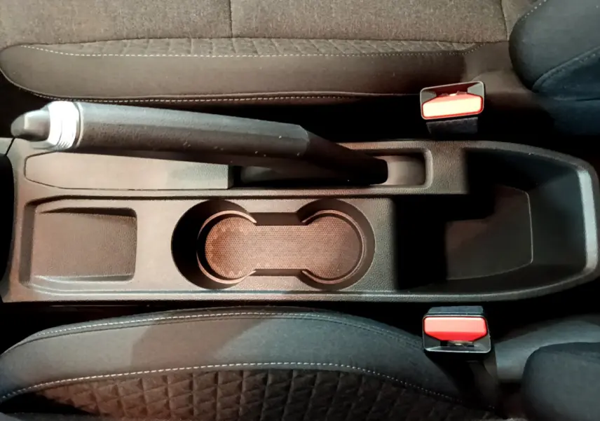 Vue plongeante sur la console centrale noire de la Renault Clio Business TCe 100 avec frein à main manuel et porte-gobelets.