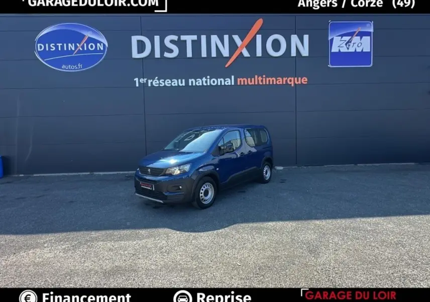 Peugeot Rifter bleu 2024 en 3/4 avant droit, version 1.5 BlueHDi 100 S&S Taille M Allure, stationné devant un mur gris.