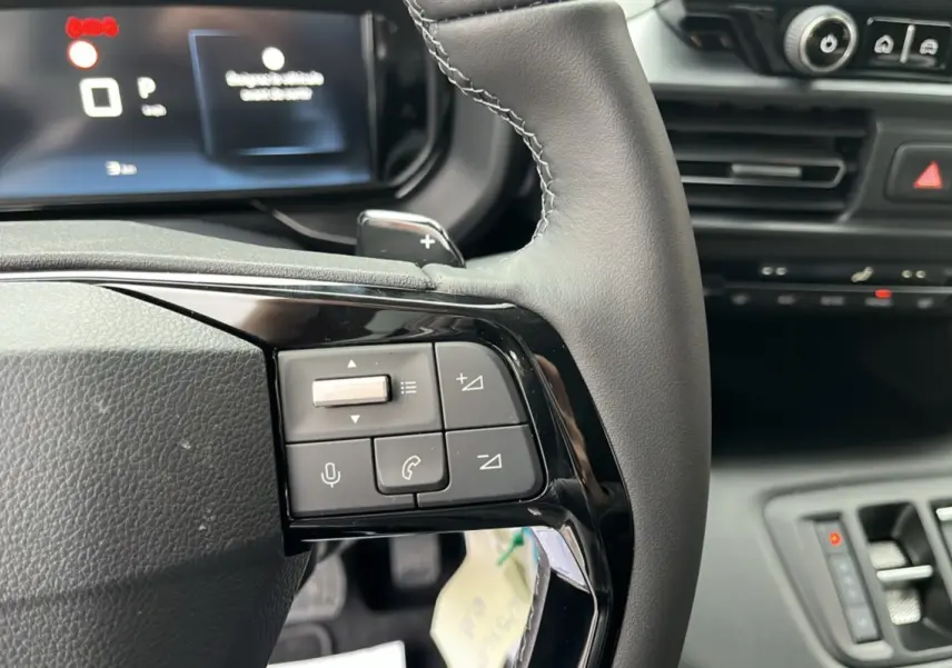 Gros plan sur le volant cuir noir multifonctions du Citroën Berlingo 2026 avec commandes audio et écran digital en arrière-plan.