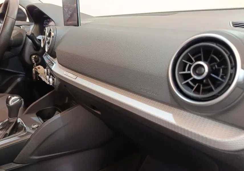 Vue intérieure côté passager de l’Audi Q2 35 TFSI 2022, tableau de bord gris foncé avec aérateurs ronds chromés.
