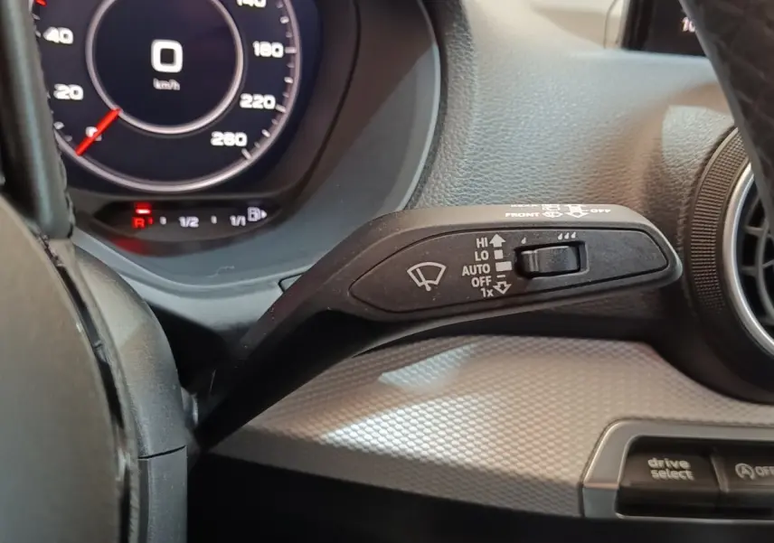 Gros plan sur la commande d'essuie-glace à gauche du volant dans l'Audi Q2 gris foncé, tableau de bord digital visible.