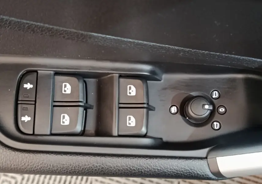 Gros plan sur les commandes de lève-vitres et réglage des rétroviseurs côté conducteur de l’Audi Q2 gris foncé 2022.