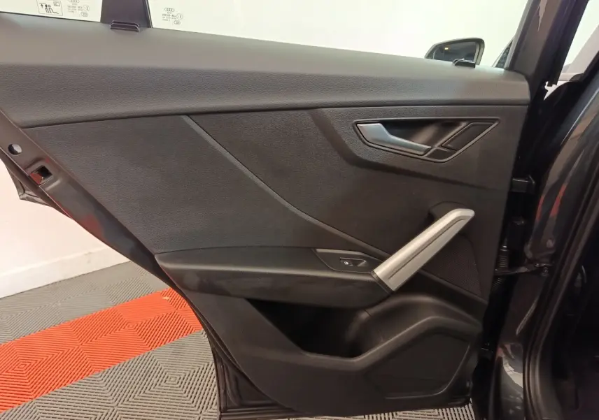 Vue intérieure de la porte arrière droite gris foncé de l'Audi Q2 35 TFSI 150 S Tronic Business Line avec poignée argentée.