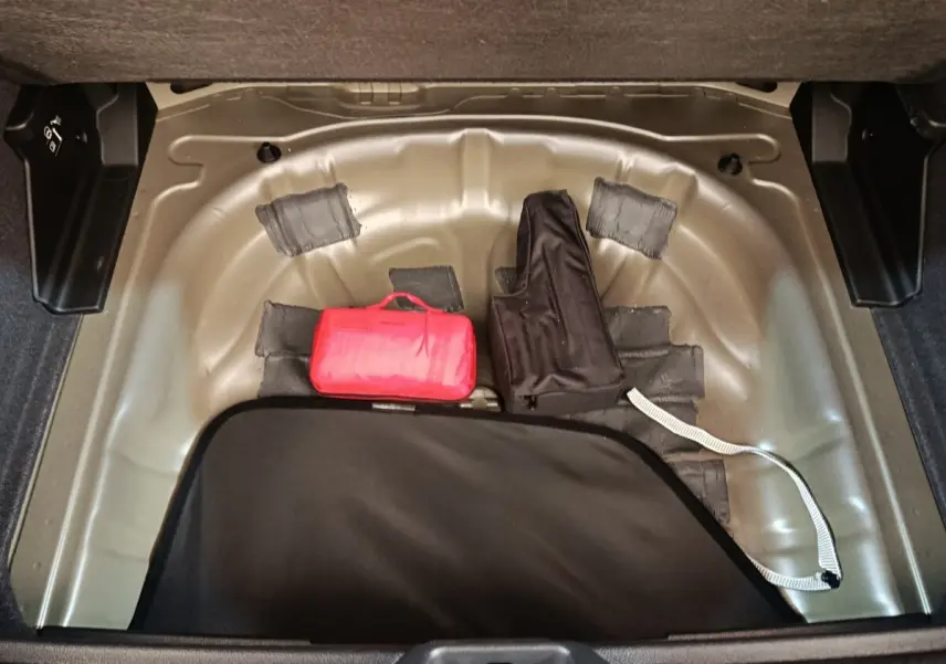 Coffre ouvert d’Audi Q2 gris foncé, vue plongeante sur espace de rangement avec trousse de secours rouge et housse noire.
