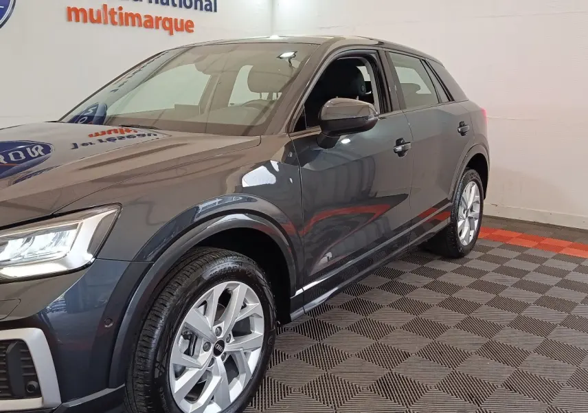Audi Q2 gris foncé vue 3/4 avant droit, avec jantes alliage et rétroviseur côté conducteur visible.