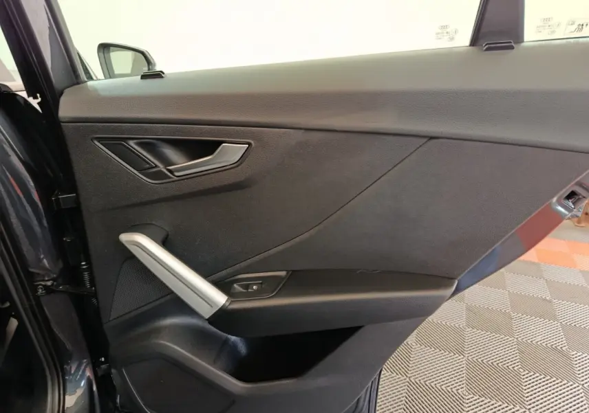 Vue intérieure côté gauche de la porte avant gris foncé de l'Audi Q2 avec poignée argentée et commande de vitre.