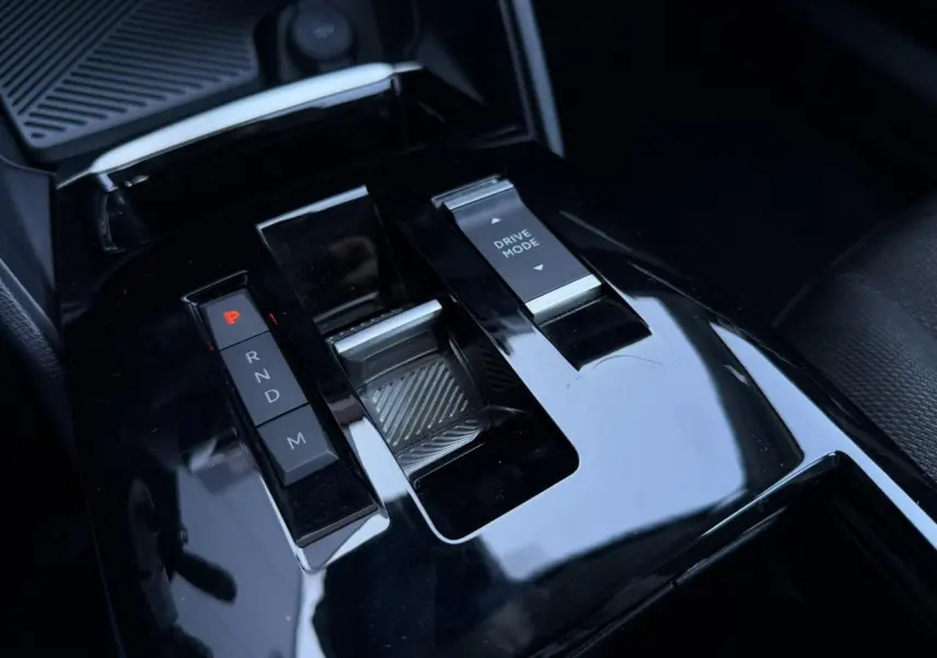 Gros plan sur la console centrale noire brillante de la Citroën C4 Hybrid 2025 avec sélecteur de boîte auto et commande Drive Mode.
