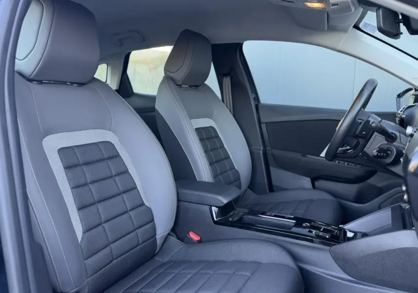 Vue intérieure côté gauche montrant les sièges avant gris et noir avec accoudoir central et tableau de bord partiel de la Citroën C4 Hybrid 2025.