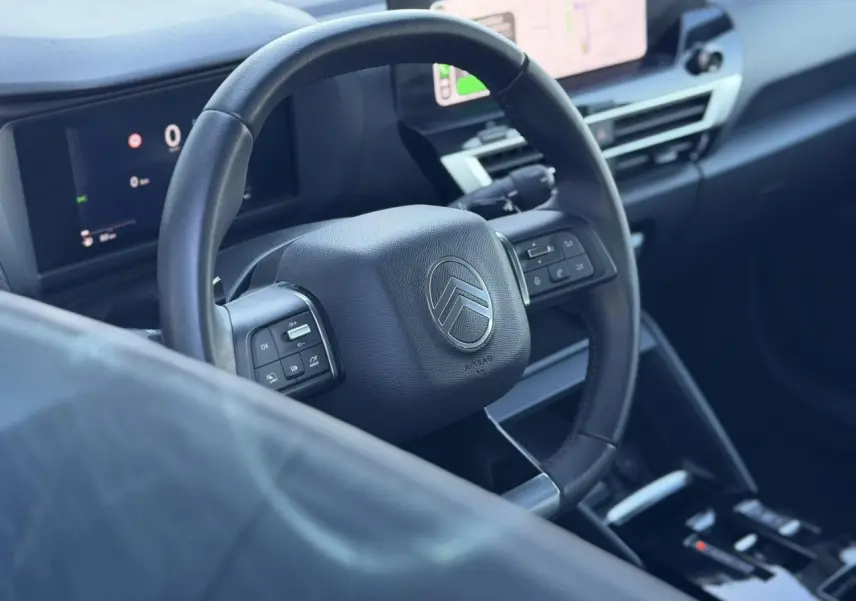 Vue intérieure rapprochée du volant cuir noir et du tableau de bord numérique de la Citroën C4 Hybrid 2025.