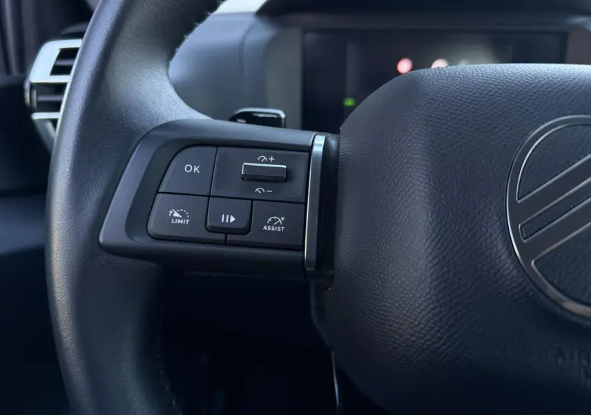 Gros plan sur le volant noir de la Citroën C4 Hybrid 145, avec commandes intégrées côté gauche et logo central.