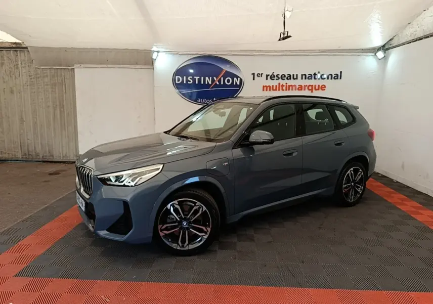 BMW X1 xDrive25e M Sport gris foncé vue 3/4 avant droit en intérieur sur sol noir et rouge.