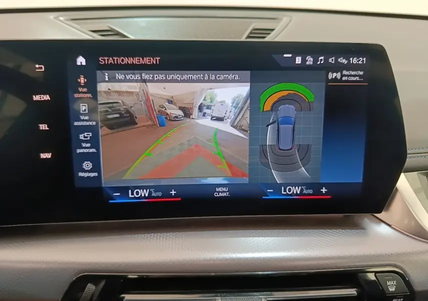 Écran tactile central du BMW X1 xDrive25e M Sport 2023 montrant l'aide au stationnement avec vue caméra arrière et capteurs.