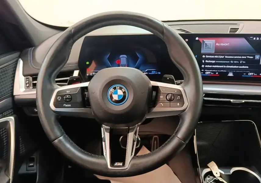 Vue rapprochée du volant cuir et alu multifonctions d’une BMW X1 xDrive25e M Sport 2023, tableau de bord digital visible.