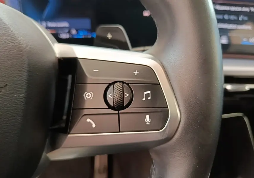 Gros plan sur le volant multifonctions en cuir et alu du BMW X1 xDrive25e M Sport 2023, boutons de contrôle visibles.