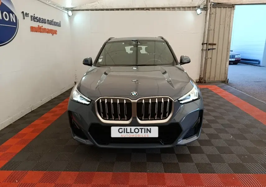Vue frontale d'un BMW X1 xDrive25e M Sport gris foncé avec calandre imposante et phares LED allumés dans un garage.