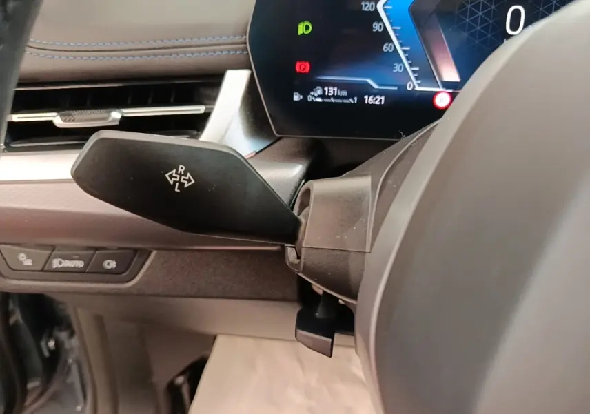 Gros plan sur le commodo de clignotant à gauche du volant cuir alu, tableau de bord digital d'une BMW X1 xDrive25e M Sport gris foncé 2023.