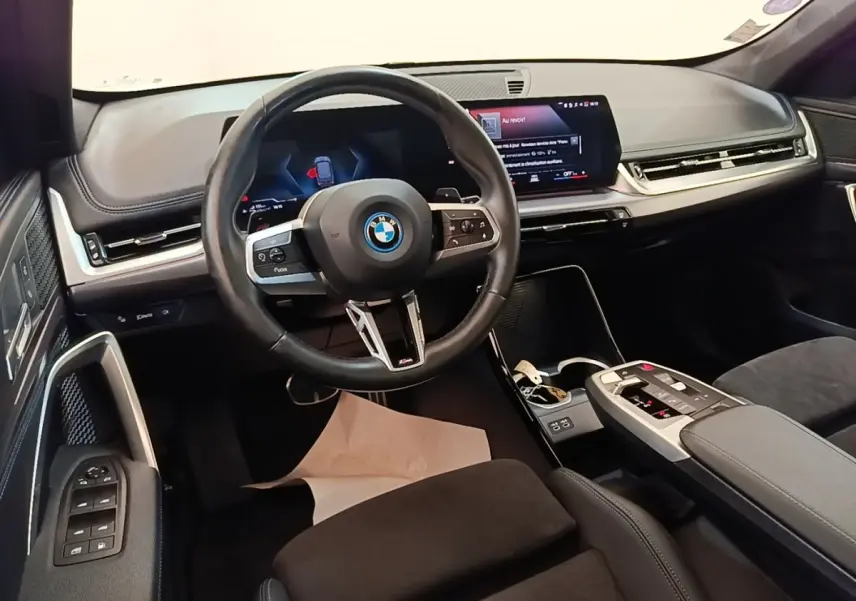 Vue intérieure du poste de conduite BMW X1 xDrive25e M Sport 2023, volant cuir alu et écran tactile large.