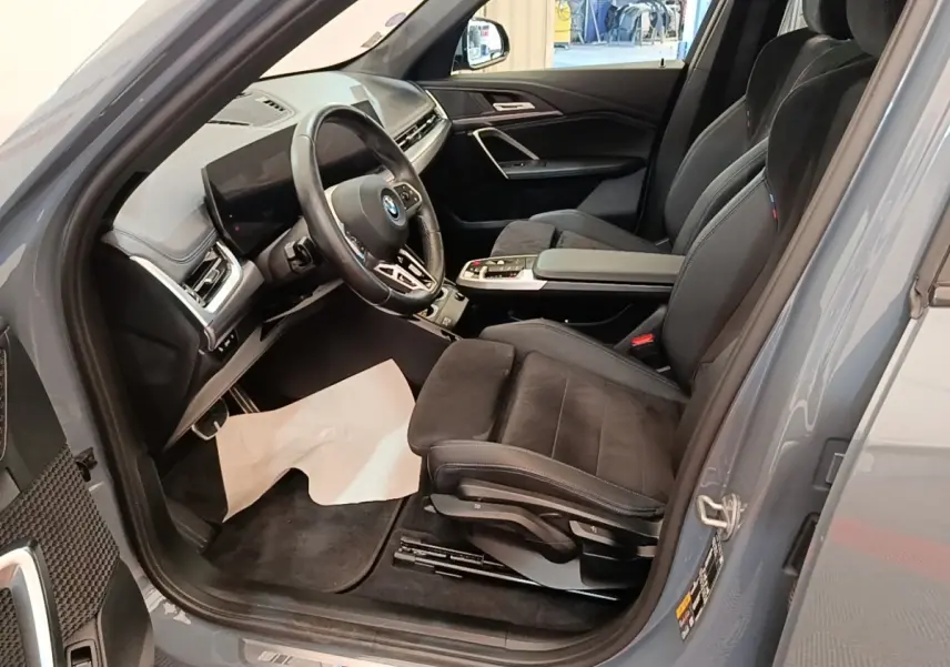 Vue intérieure côté conducteur du BMW X1 xDrive25e M Sport gris foncé, volant cuir alu multifonctions et sièges sport noirs.