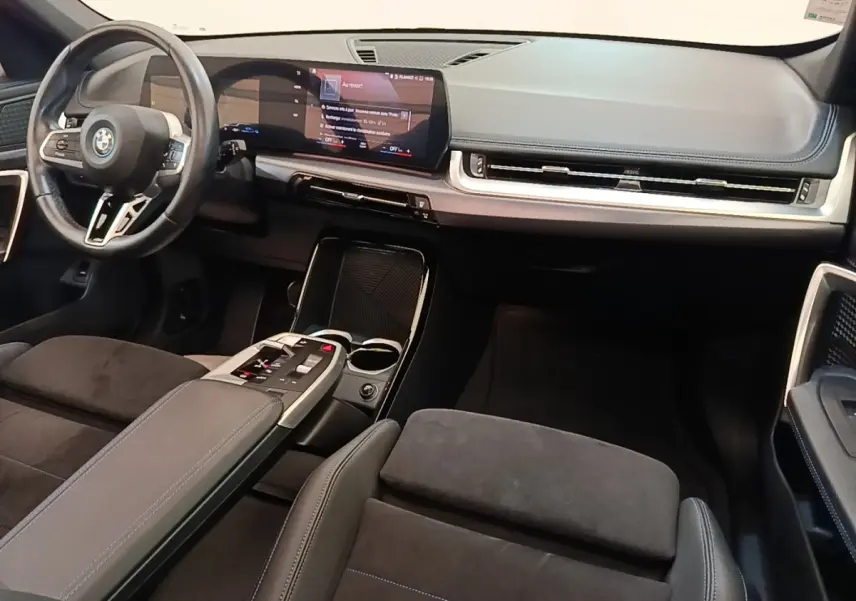 Intérieur BMW X1 xDrive25e M Sport 2023, vue avant côté conducteur, tableau de bord noir avec écran tactile large.