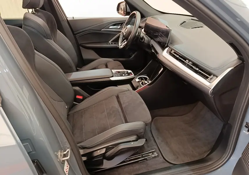 Intérieur côté conducteur BMW X1 xDrive25e M Sport 2023, sièges gris foncé et tableau de bord moderne avec écran tactile.
