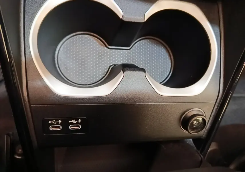 Gros plan sur les ports USB-C et prise 12V sous les porte-gobelets noirs d’un BMW X1 xDrive25e gris foncé.