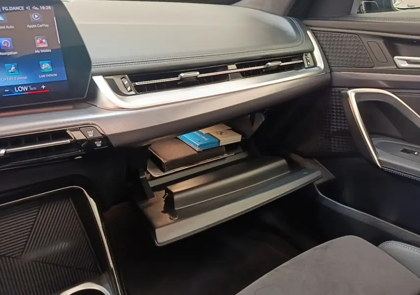 Intérieur BMW X1 xDrive25e M Sport 2023, vue côté passager sur boîte à gants ouverte avec tableau de bord gris foncé.