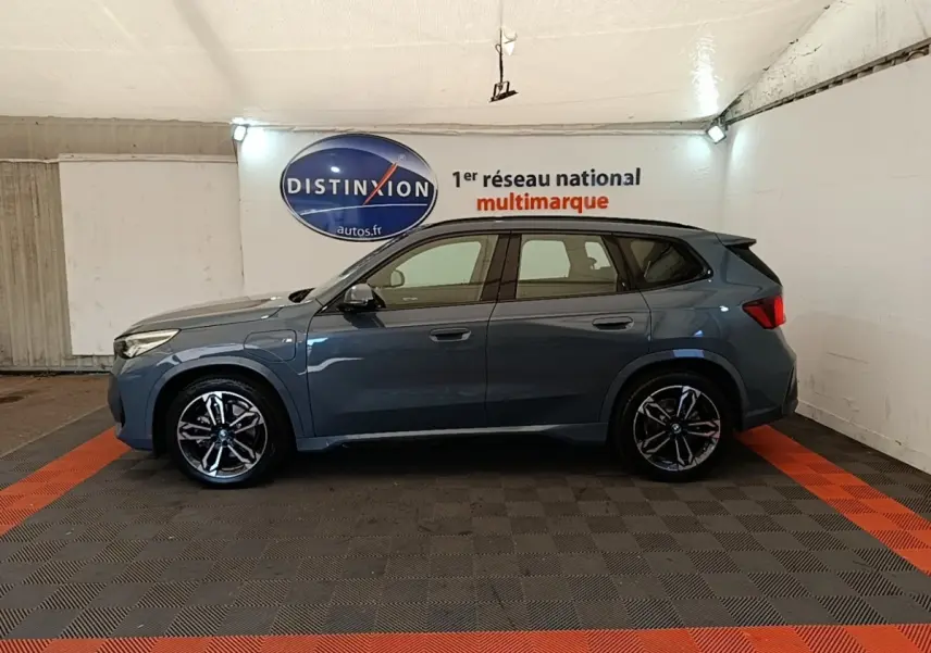 Vue de profil côté gauche d’un BMW X1 xDrive25e M Sport gris foncé, avec jantes alliage et prises de recharge visibles.
