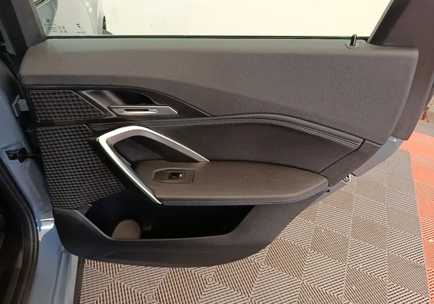 Vue intérieure côté gauche de la porte arrière grise du BMW X1 xDrive25e M Sport 2023 avec garniture noire et surpiqûres bleues.