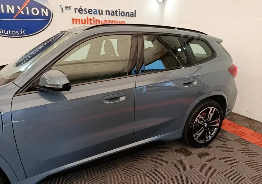 Vue latérale droite d’un BMW X1 xDrive25e M Sport gris foncé avec jantes noires et toit noir en intérieur showroom.