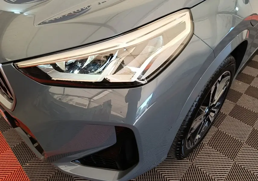 Gros plan sur l'avant droit du BMW X1 xDrive25e M Sport gris foncé, mettant en valeur le phare LED et la jante alliage.
