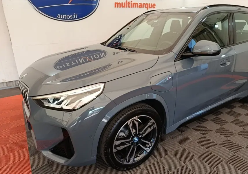 Vue 3/4 avant droit d’un BMW X1 xDrive25e M Sport gris foncé avec jantes noires et phares LED allumés.