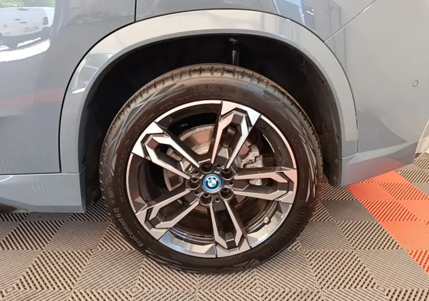 Gros plan sur la roue arrière droite d’un BMW X1 gris foncé avec jante alliage M Sport au design moderne.