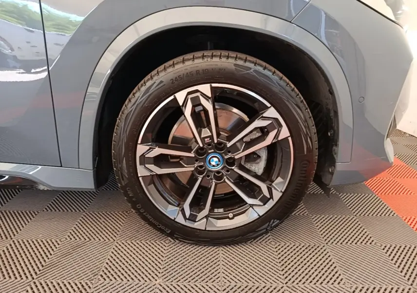 Gros plan sur la roue avant gauche d’un BMW X1 gris foncé avec jante alliage au design géométrique.