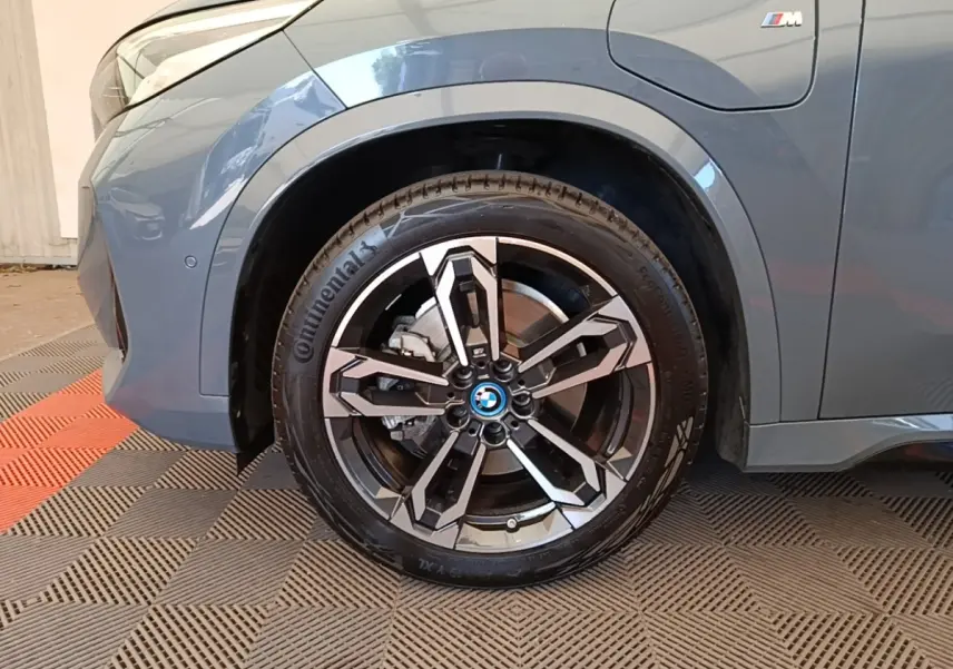 Gros plan sur la roue avant gauche et la partie latérale gris foncé du BMW X1 xDrive25e M Sport avec logo M visible.