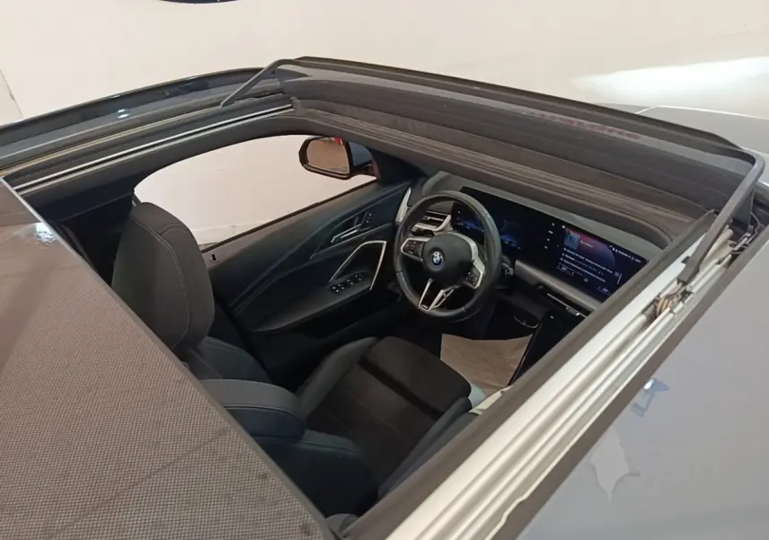 Vue intérieure par le toit ouvrant d'une BMW X1 xDrive25e M Sport gris foncé, volant multifonctions et écran tactile visible.