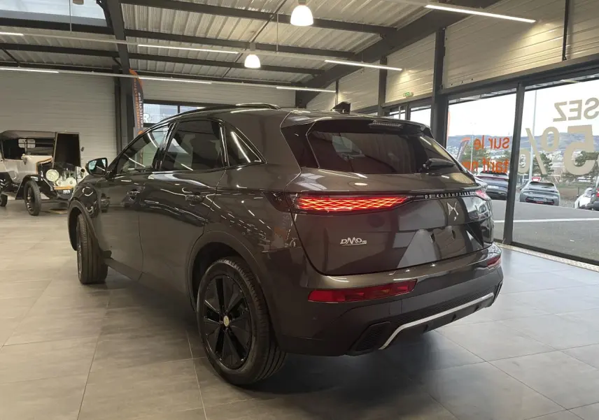 Vue 3/4 arrière droite du DS7 Crossback gris titanium avec feux arrière LED allumés en showroom.