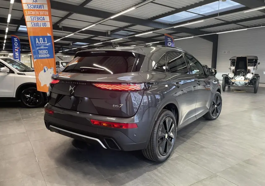 Vue 3/4 arrière droite du DS7 Crossback gris titanium avec feux arrière LED et jantes noires en showroom.