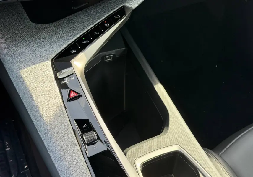 Détail de la console centrale du Peugeot 3008 2026, avec accoudoir tissu gris et commandes noires brillantes.