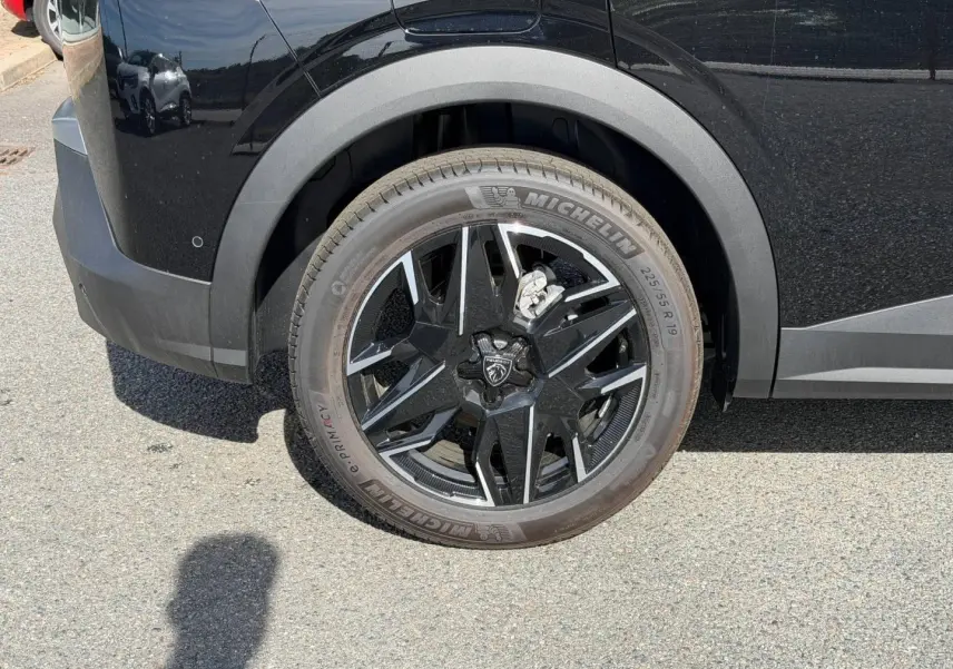 Gros plan sur la roue avant gauche d’un Peugeot 3008 noir Perla Nera avec jante alu noire et détails argentés.