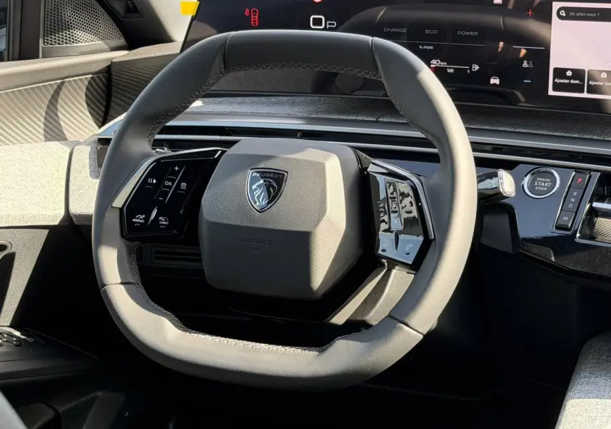 Vue rapprochée du volant cuir gris du Peugeot 3008 2026 avec commandes multifonctions et tableau de bord numérique.