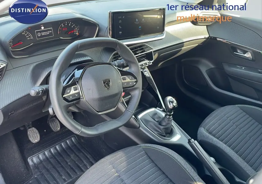 Vue intérieure côté conducteur de la Peugeot 208 1.2 PureTech 100ch Active 2024 avec volant compact et levier de vitesse manuel.